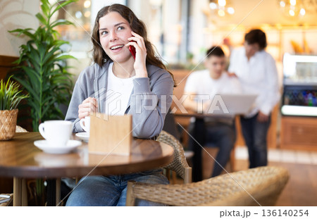 Girl in cafe drinks coffee and calling using mobile phone 136140254