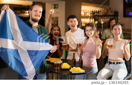 Football fans waving the flag of Scotland while drinking beer and watching tournament in sport bar 136140265