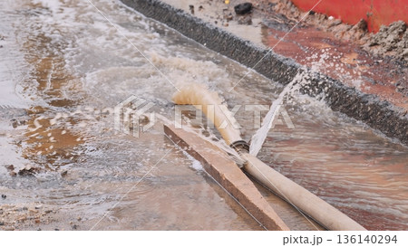 Flooding street with water gushing from a pipe laying on the ground 136140294