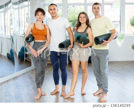 Happy portrait of four young people posing with mats, going to practicing yoga at gym 136140295