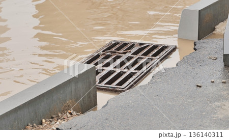 Grate overflowing with muddy stormwater on urban street after heavy rain Grate overflowing with muddy stormwater on urban street after heavy rain 136140311