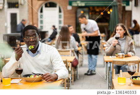 African man sits on terrace of a restaurant and eats African man sits on terrace of a restaurant and eats 136140333