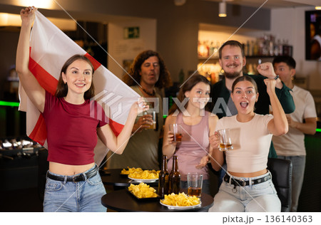 Company of fans of different ages waving flag of England and celebrating victory of favorite team in sports bar 136140363