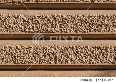 Rough stipple stucco creating horizontal bands on a sandy brown building facade Rough stipple stucco creating horizontal bands on a sandy brown building facade 136140367