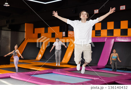 Cheerful young man in sportswear bouncing and jumping on trampolines indoors in leisure sports center indoors 136140432