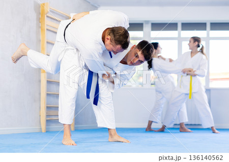 Men practice grabbing and throwing on sports mats during judo training 136140562
