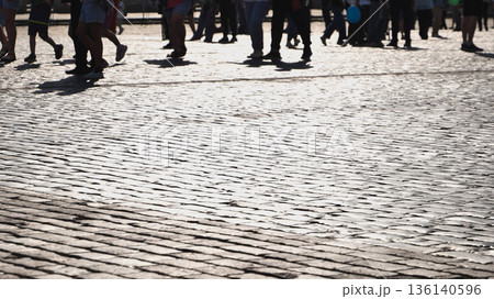 Crowd of people walking on cobblestone street creating shadows in bright sunlight Crowd of people walking on cobblestone street creating shadows in bright sunlight 136140596