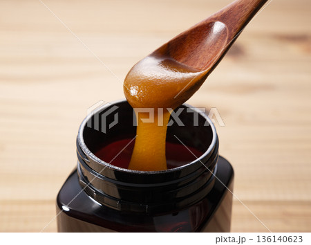 黒いボトルから木のスプーンですくった濃厚なマヌカハニー（遮光瓶・クローズアップ） 136140623
