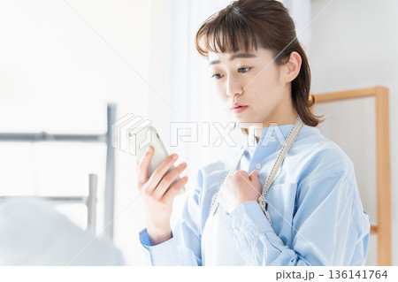 家事をしながらスマホを見る若い女性 家事をしながらスマホを見る若い女性 136141764