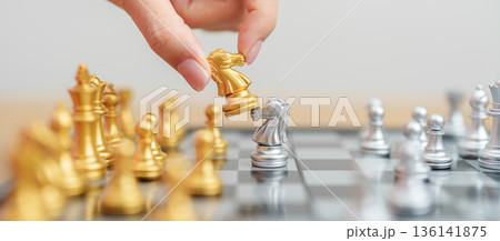 hand moving gold Chess knight figure and Checkmate opponent during chessboard competition. Strategy, Success, management, business planning, win, disruption, Trade war and leadership concept 136141875