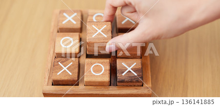 Hand holding and playing wooden block of tic tac toe game. A completed game of noughts and crosses or Xs and Os game. Challenge, Competition, winning, tactic, strategy and recreation concepts Hand holding and playing wooden block of tic tac toe game. A completed game of noughts and crosses or Xs and Os game. Challenge, Competition, winning, tactic, strategy and recreation concepts 136141885