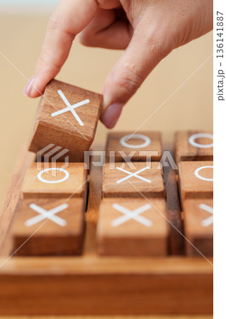 Hand holding and playing wooden block of tic tac toe game. A completed game of noughts and crosses or Xs and Os game. Challenge, Competition, winning, tactic, strategy and recreation concepts 136141887