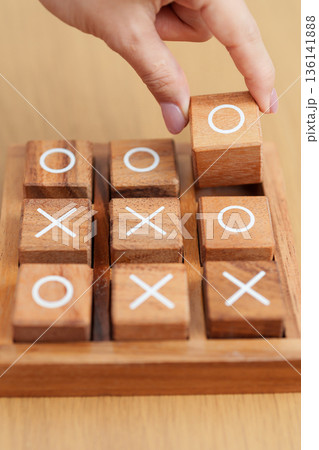 Hand holding and playing wooden block of tic tac toe game. A completed game of noughts and crosses or Xs and Os game. Challenge, Competition, winning, tactic, strategy and recreation concepts Hand holding and playing wooden block of tic tac toe game. A completed game of noughts and crosses or Xs and Os game. Challenge, Competition, winning, tactic, strategy and recreation concepts 136141888