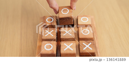 Hand holding and playing wooden block of tic tac toe game. A completed game of noughts and crosses or Xs and Os game. Challenge, Competition, winning, tactic, strategy and recreation concepts 136141889