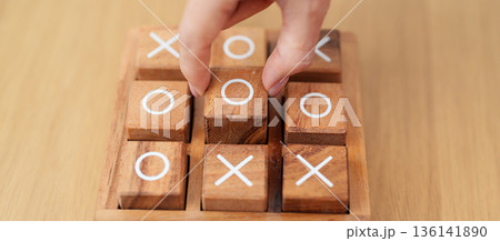 Hand holding and playing wooden block of tic tac toe game. A completed game of noughts and crosses or Xs and Os game. Challenge, Competition, winning, tactic, strategy and recreation concepts 136141890