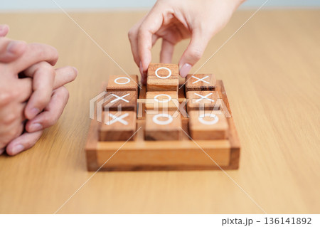 Hand holding and playing wooden block of tic tac toe game. A completed game of noughts and crosses or Xs and Os game. Challenge, Competition, winning, tactic, strategy and recreation concepts 136141892