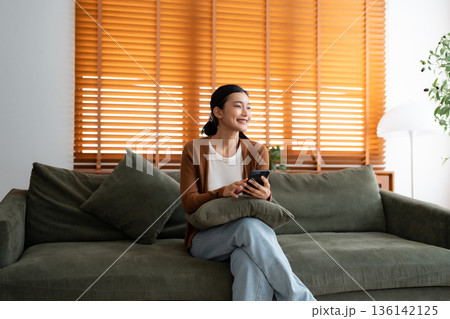 Happy young asian woman relax on comfortable couch at home texting messaging on smartphone Happy young asian woman relax on comfortable couch at home texting messaging on smartphone 136142125