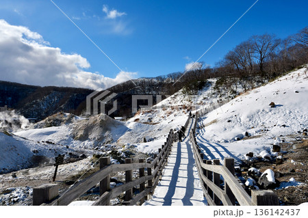 冬晴れの「登別地獄谷」雪と茶色い山肌の中を走る遊歩道 136142437