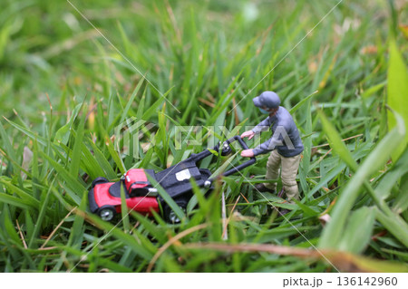 Miniature Worker Pushing Lawn Mower Through Green Grass 136142960