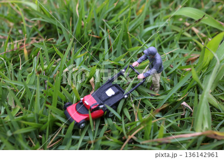 Miniature Worker Pushing Lawn Mower Through Green Grass Miniature Worker Pushing Lawn Mower Through Green Grass 136142961