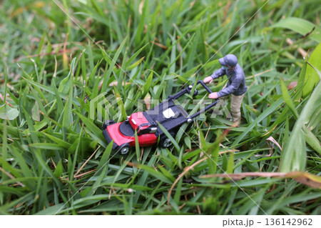Miniature Worker Pushing Lawn Mower Through Green Grass Miniature Worker Pushing Lawn Mower Through Green Grass 136142962