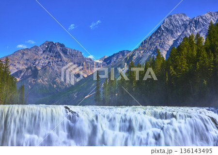 Wapta Falls Rushing Waterfall with Mountain Peaks and Pine Forest Under Clear Blue Sky Wapta Falls Rushing Waterfall with Mountain Peaks and Pine Forest Under Clear Blue Sky 136143495
