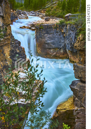 Waterfall and Turquoise River Flowing Through Rocky Canyon in Lush Forest 136143525