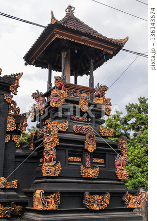 Balinese Hindu temple shrine with ornate gold carvings against a cloudy sky for travel concept 136143674