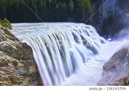 Powerful Waterfall Flowing Over Rocky Cliff With Lush Forest In Background 136143704