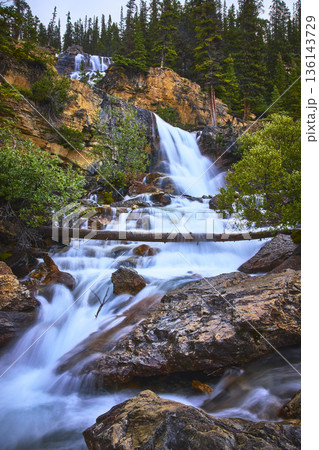 Waterfall Cascading Over Rocky Cliff with Flowing Water and Evergreen Forest 136143729