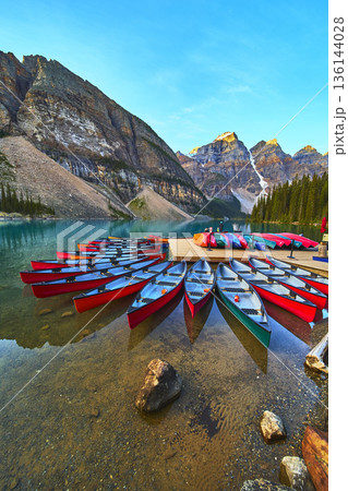 Canoes on Crystal Clear Lake at Sunrise with Rocky Mountains and Evergreen Forest 136144028