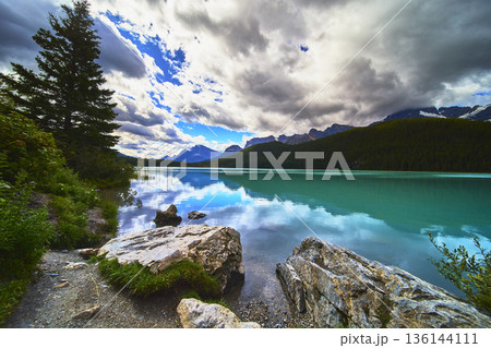 Turquoise Lake with Rocky Shore and Pine Trees against Mountain Backdrop Turquoise Lake with Rocky Shore and Pine Trees against Mountain Backdrop 136144111