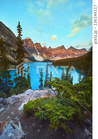 Lake Moraine Sunrise Mountain Peaks and Turquoise Water with Pine Trees 136144117