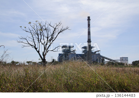 Power plant rising above dry grass under a cloudy sky with natural light, conveying energy production in an environmental context 136144483