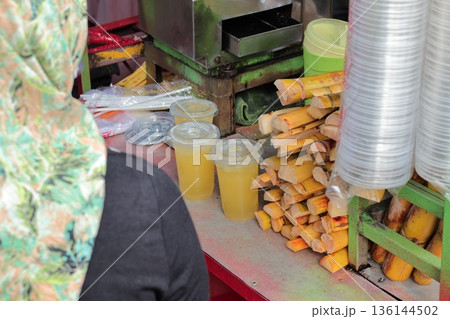 Indonesian Sugar Cane Juice Vendor Preparing Refreshments with Natural Light for Local Street Food Experience 136144502