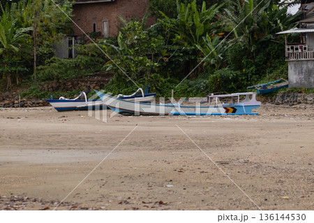 Traditional fishing boats resting on sand beach shoreline with tropical jungle background and village houses. 136144530