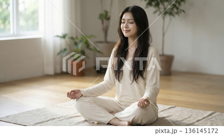 部屋で胡座をかき目を閉じて瞑想するリラックスした日本人女性 136145172