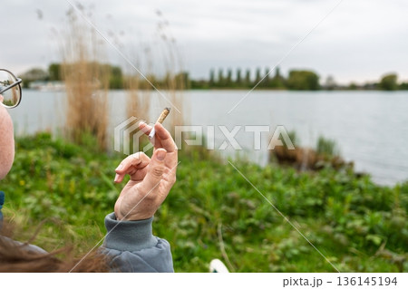 Contemplative Moment Woman Smoking by the Serene Lake, Enjoying Nature s Tranquility 136145194