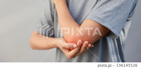 Close-up of woman hand holding painful injured elbow with red inflamed spot. Concept of joint bone pain, muscle injury, arthritis, tendonitis, or ache from sports or work in outdoor background. 136145526
