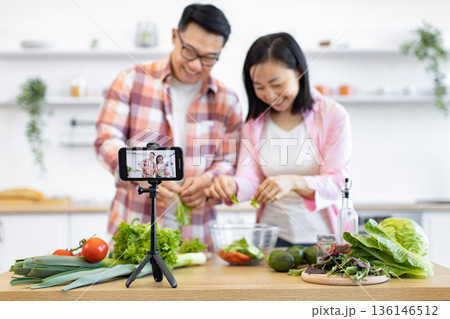 An Asian couple is preparing a healthy salad in their kitchen while recording a video for their online audience 136146512