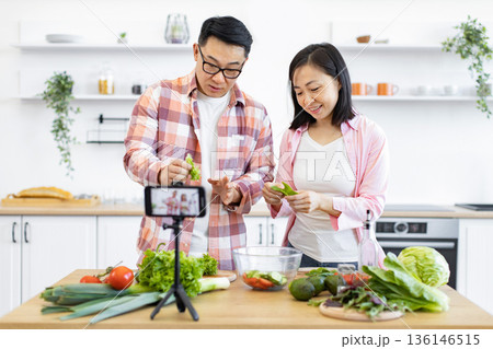 A happy couple prepares a meal in their kitchen, filming a cooking tutorial for their online audience A happy couple prepares a meal in their kitchen, filming a cooking tutorial for their online audience 136146515