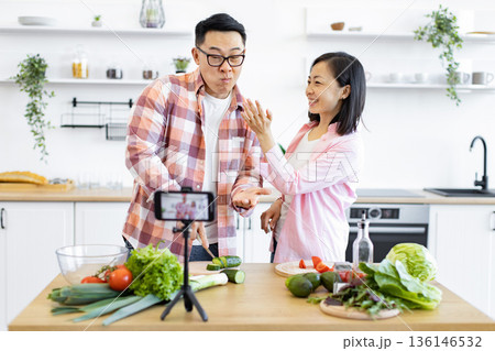 An Asian couple is filming a cooking video in their bright, modern kitchen, preparing fresh vegetables for a healthy meal 136146532