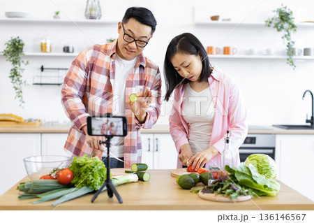 A couple prepares a meal together while recording a cooking video for their online audience A couple prepares a meal together while recording a cooking video for their online audience 136146567