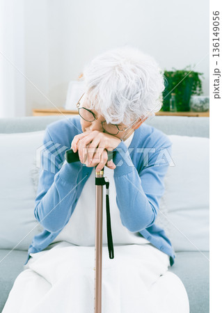 リビングで杖を手に落ち込むシニア女性 リビングで杖を手に落ち込むシニア女性 136149056