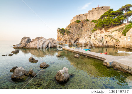 Dubrovnik old city small west harbor with boats. Near is the Lovrijenac fortress. Summer weather, morning soft light. Part of UNESCO heritage. Dubrovnik old city small west harbor with boats. Near is the Lovrijenac fortress. Summer weather, morning soft light. Part of UNESCO heritage. 136149727