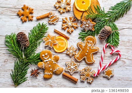Christmas gingerbread and sweets are placed on wooden desk. Cookies and sweet food in shape of stars and snow flakes. Winter theme, rustic style. Pine trees on the side. Candy stick and other spice. Christmas gingerbread and sweets are placed on wooden desk. Cookies and sweet food in shape of stars and snow flakes. Winter theme, rustic style. Pine trees on the side. Candy stick and other spice. 136149850