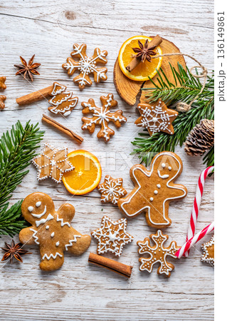 Christmas gingerbread and sweets are placed on wooden desk. Cookies and sweet food in shape of stars and snow flakes. Winter theme, rustic style. Pine trees on the side. Candy stick and other spice. 136149861