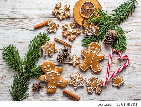 Christmas gingerbread and sweets are placed on wooden desk. Cookies and sweet food in shape of stars and snow flakes. Winter theme, rustic style. Pine trees on the side. Candy stick and other spice. 136149881