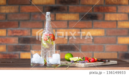 Refreshment drink with strawberry and lime placed on wooden desk. Two glasses with ice. Brick wall background. 136149933