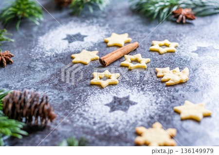 Christmas sweets and cookies in form of christmas tree placed on gray desk with pine cone and branch on the side. Winter and christmas decorations, cinnamon, sugar and star anise. 136149979